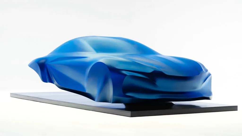 Mavi ipek örtü altında sergilenen Alpine a110 konsept heykelinin stüdyo ortamındaki görünümü